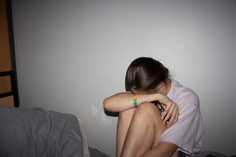 A girl with her head in her knees against a wall, with harsh flash lighting.