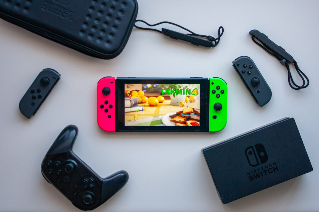 Flat layout of a Nintendo Switch game console playing Pikmin 4, surrounded by Nintendo Switch controllers, dock, and case.