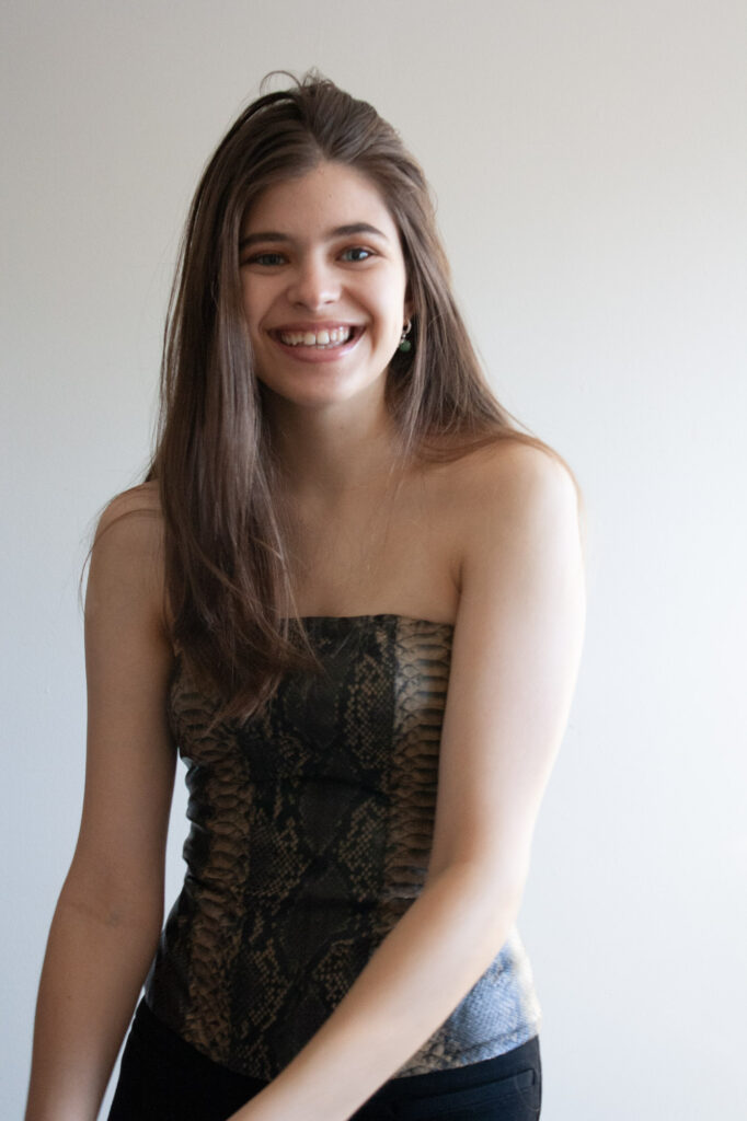 Woman wearing snakeskin top with long hair smiling and laughing with a white background.